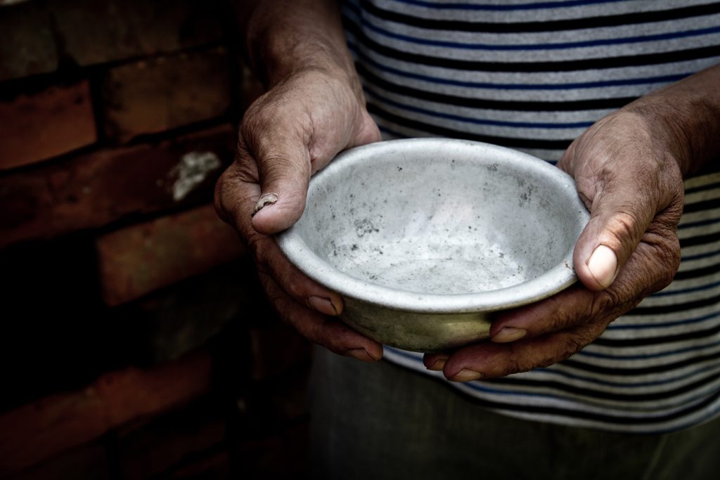 Two roughened hands hold a dirty silver bowl.