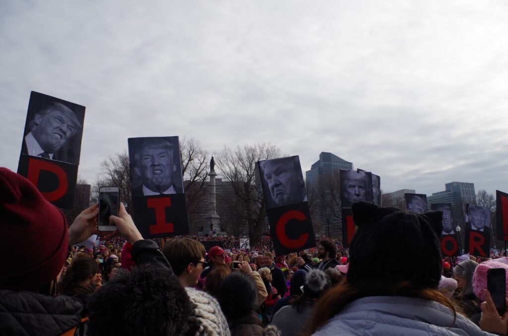 Trump's face on protest signs that say DICKTATOR