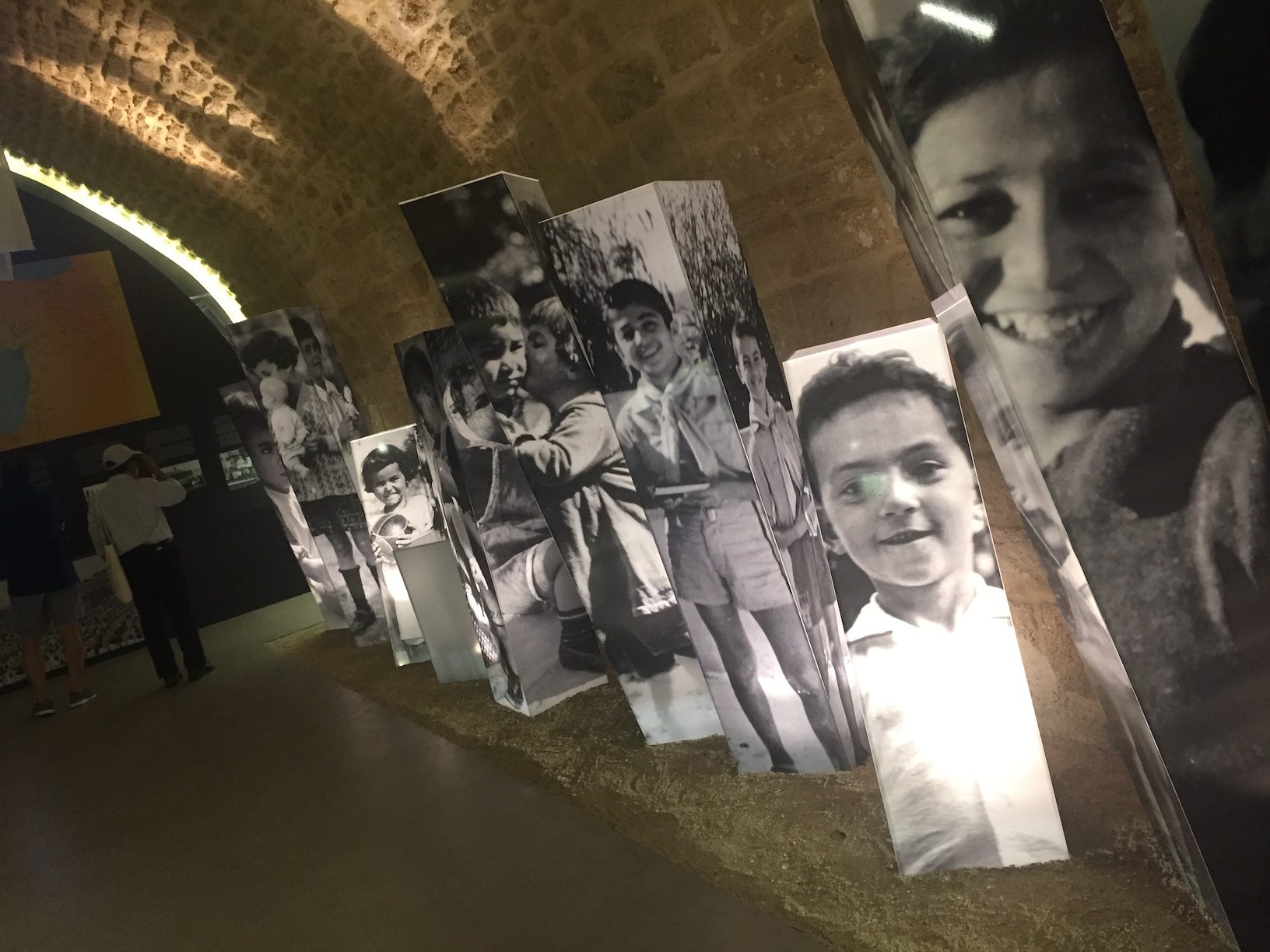 Black and white illuminated photos of smiling children in a dark exhibition.