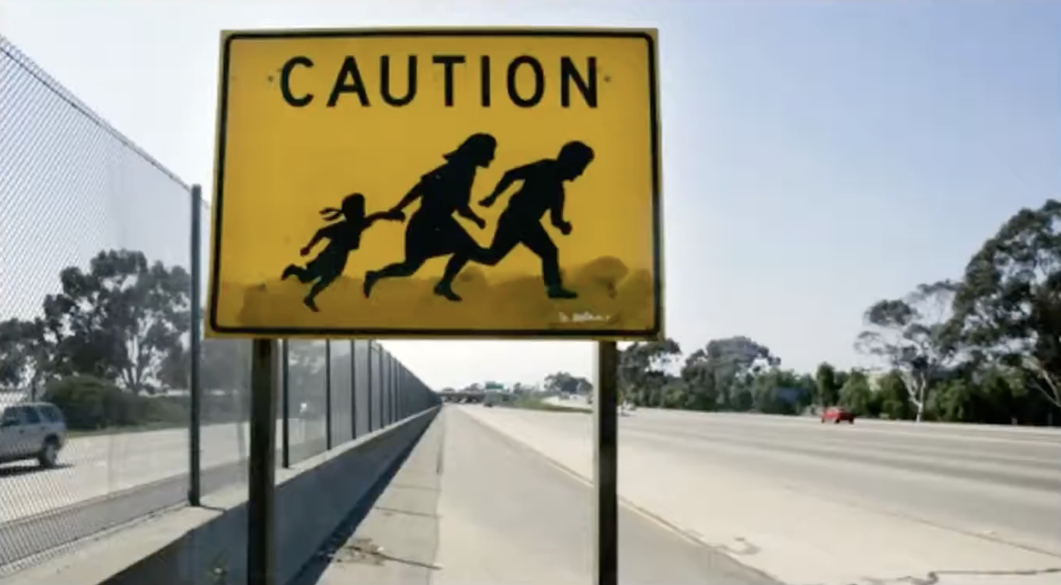 Yellow roadside sign with black figures of man, woman and child running, text, "Caution."