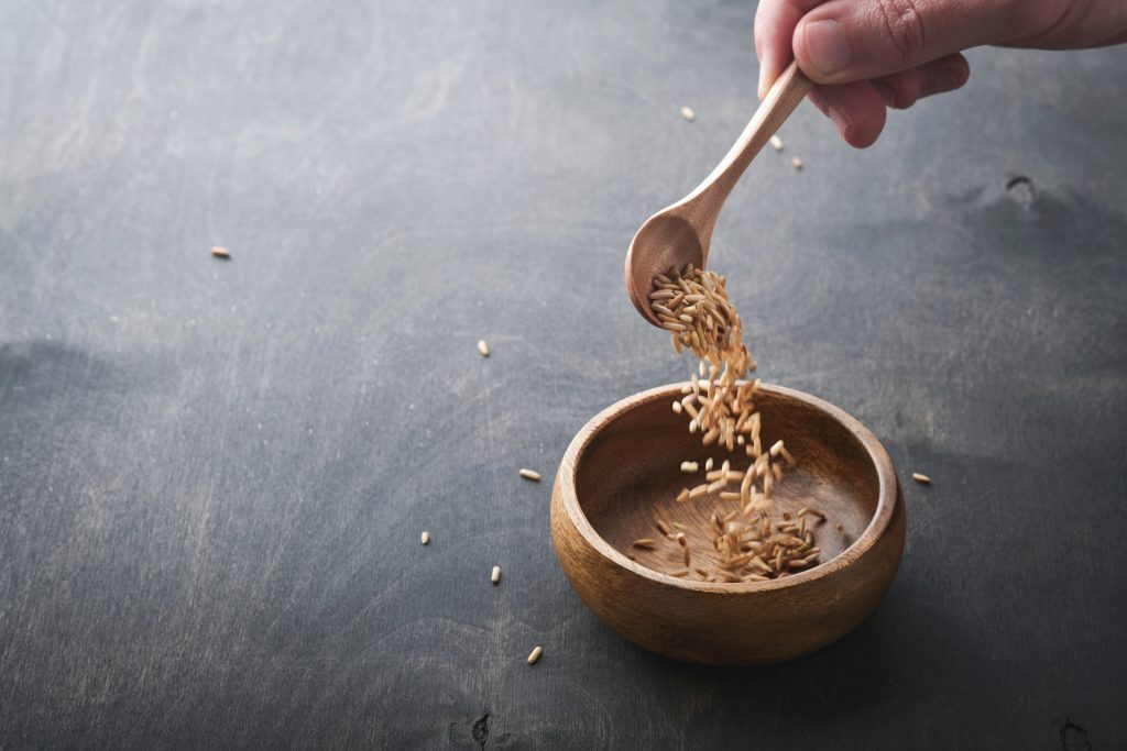 grains of rice falling from a spoon into wooden bowl