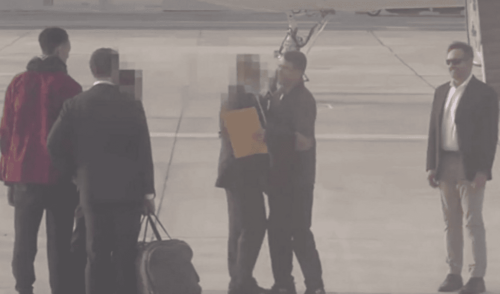 Grainy security camera image of a group of five people on a tarmac near a plane.