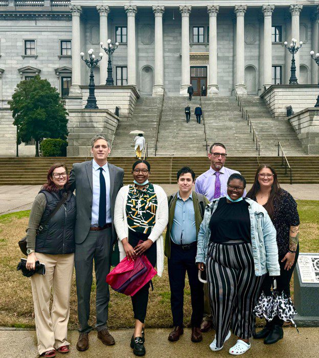 Photo of group of people standing in front of an official looking building with columns.