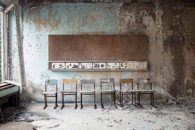 A row of chairs in front of a chalkboard in a debris-strewn school