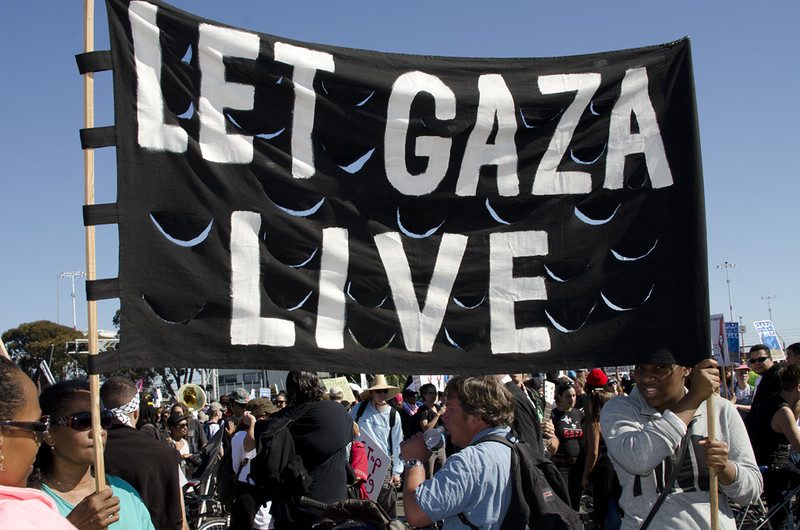 Crowd of people hold a banner that says, "Let Gaza Live."