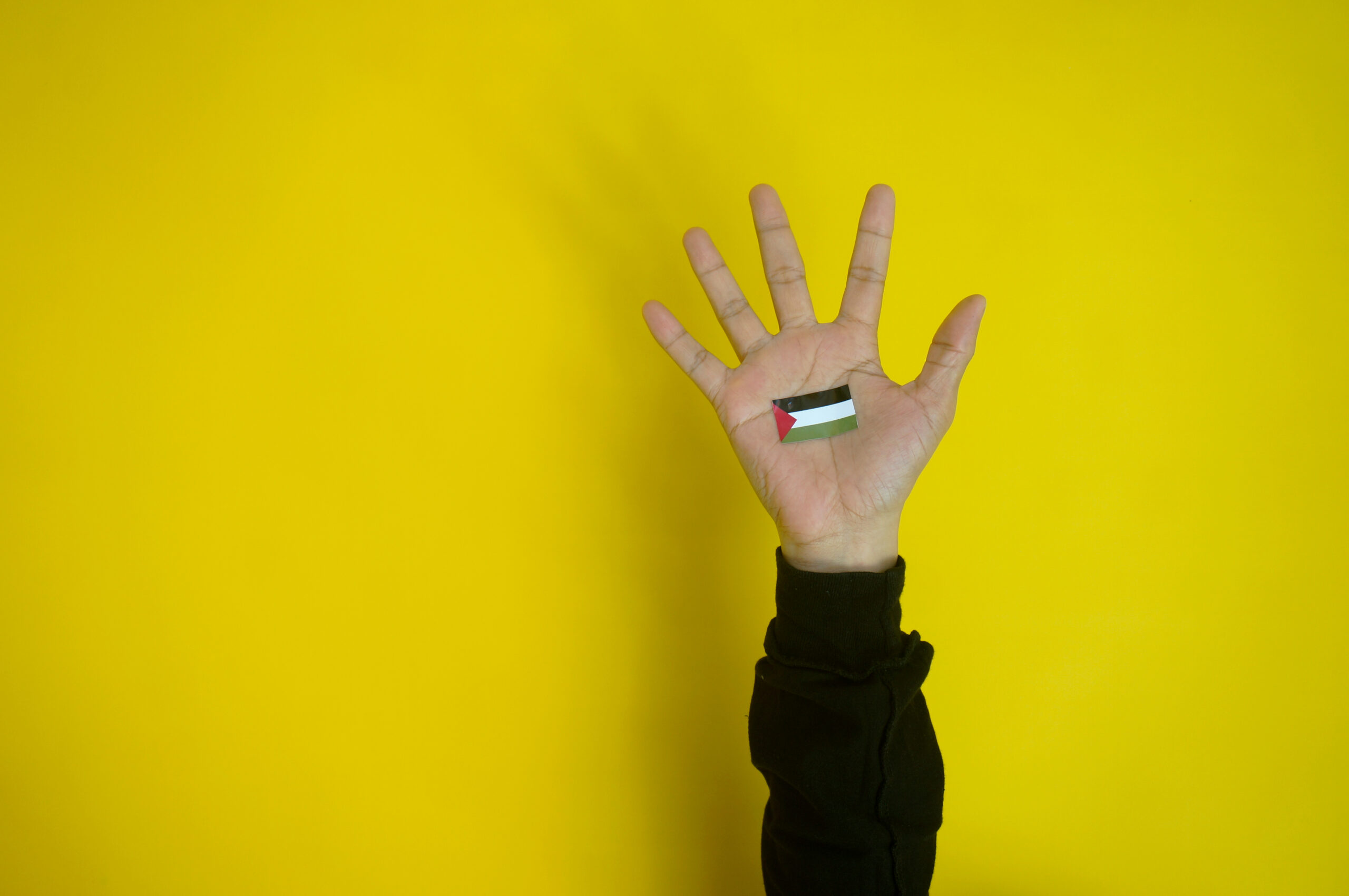 Palestine flag on hand as symbol of support and solidarity isolated over yellow background