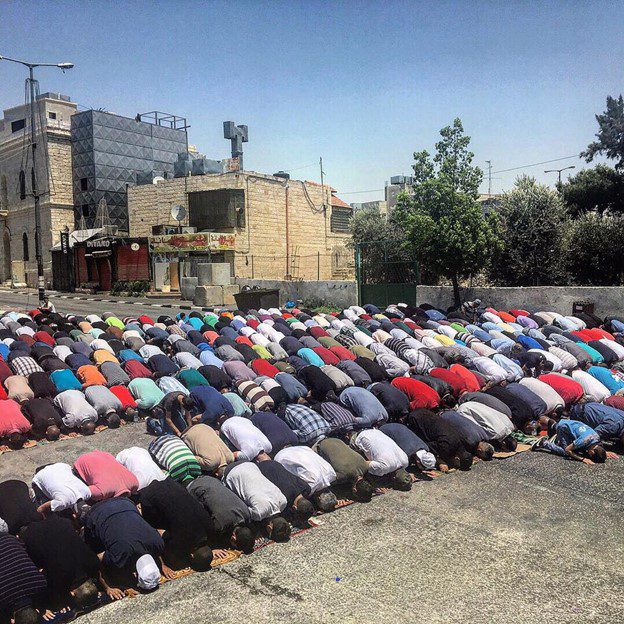 large group praying in street with buildings in background