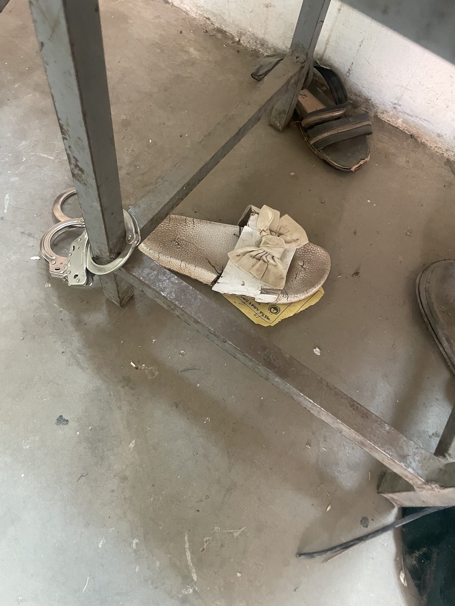 Women’s shoes left at the museum, near a metal chair, with handcuffs.