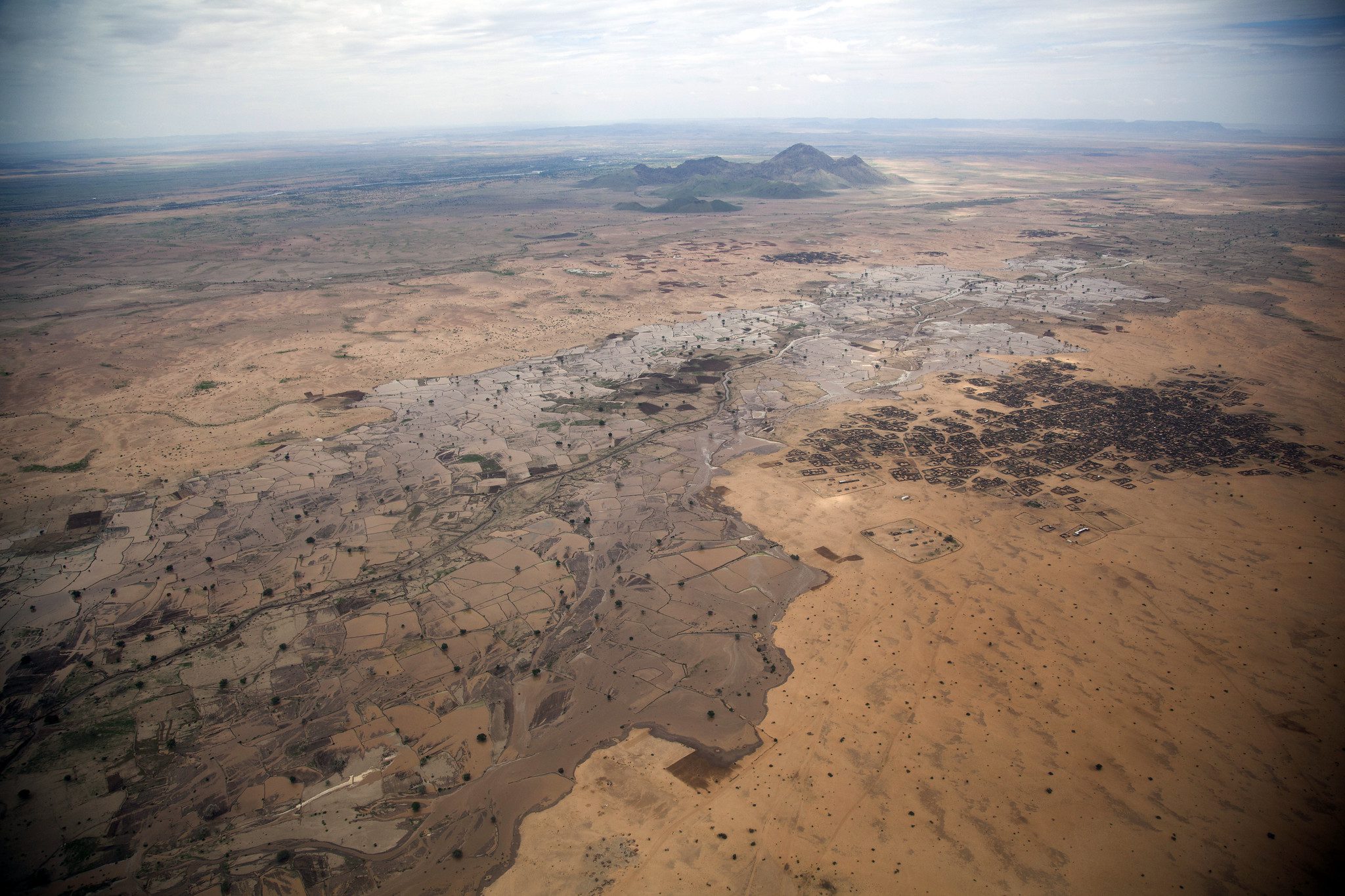 aerial photograph view over flat land with sparse trees and some hills in distance.