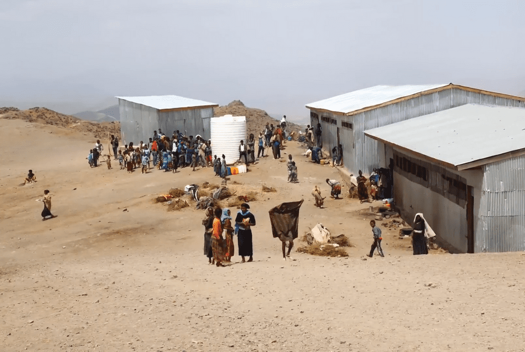 photo of displaced Ethiopians in camp gathering near 3 small buildings