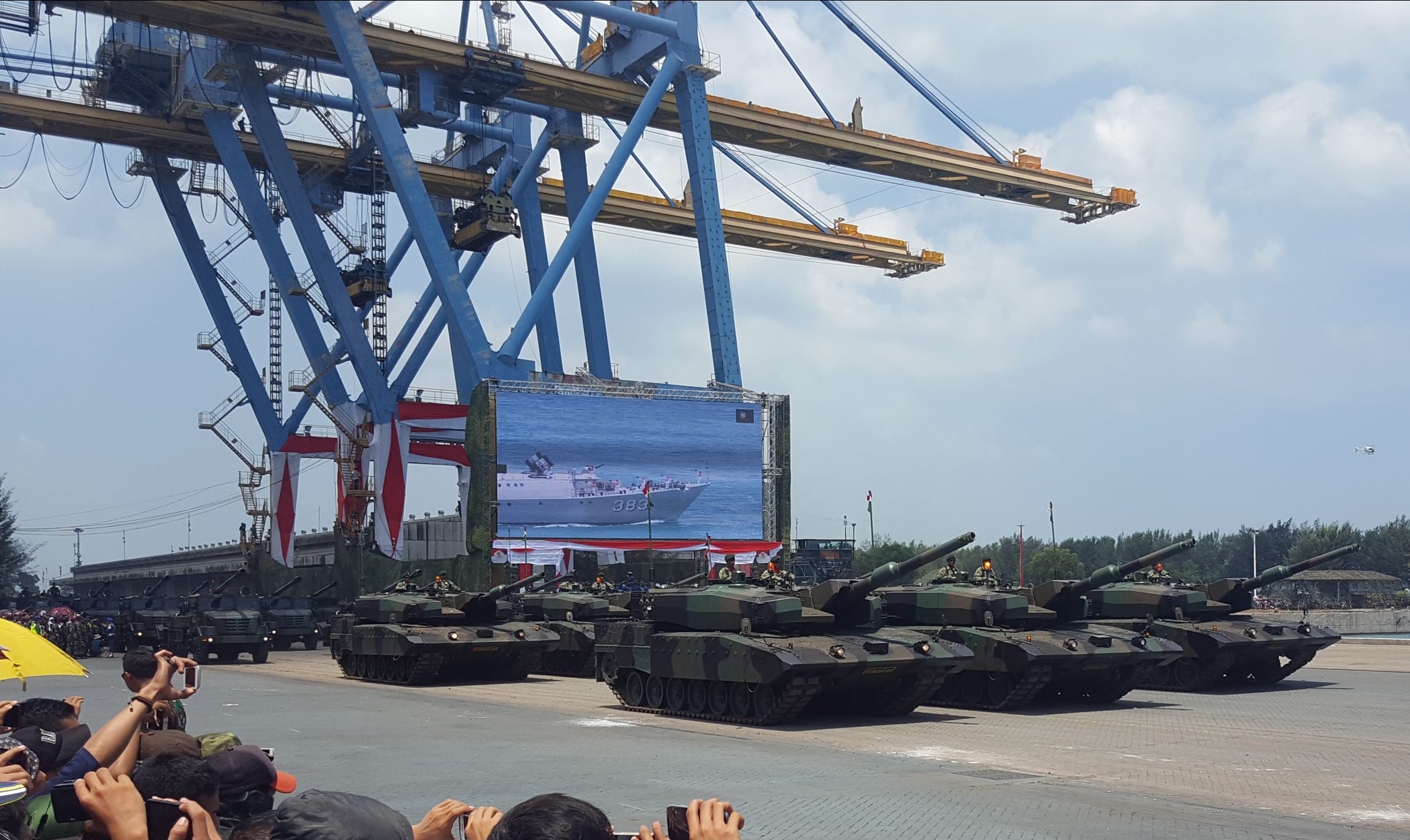 photo of several rows of army equiptment, tanks in the front and a crowd with cameras