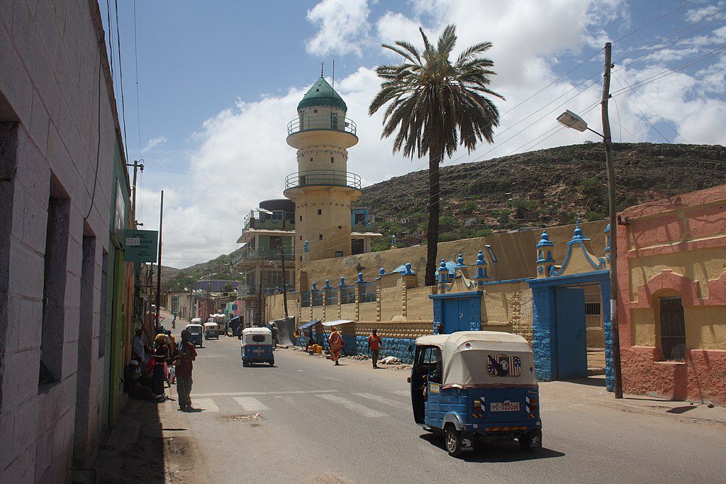 photo city street and mosque with colorful buildings along one side and a hill in the background
