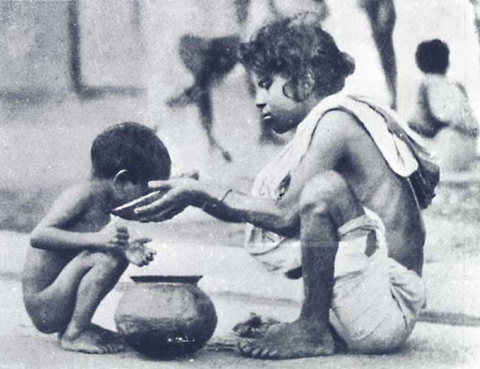 black and white photo of hungry children, one feeding another with a bowl