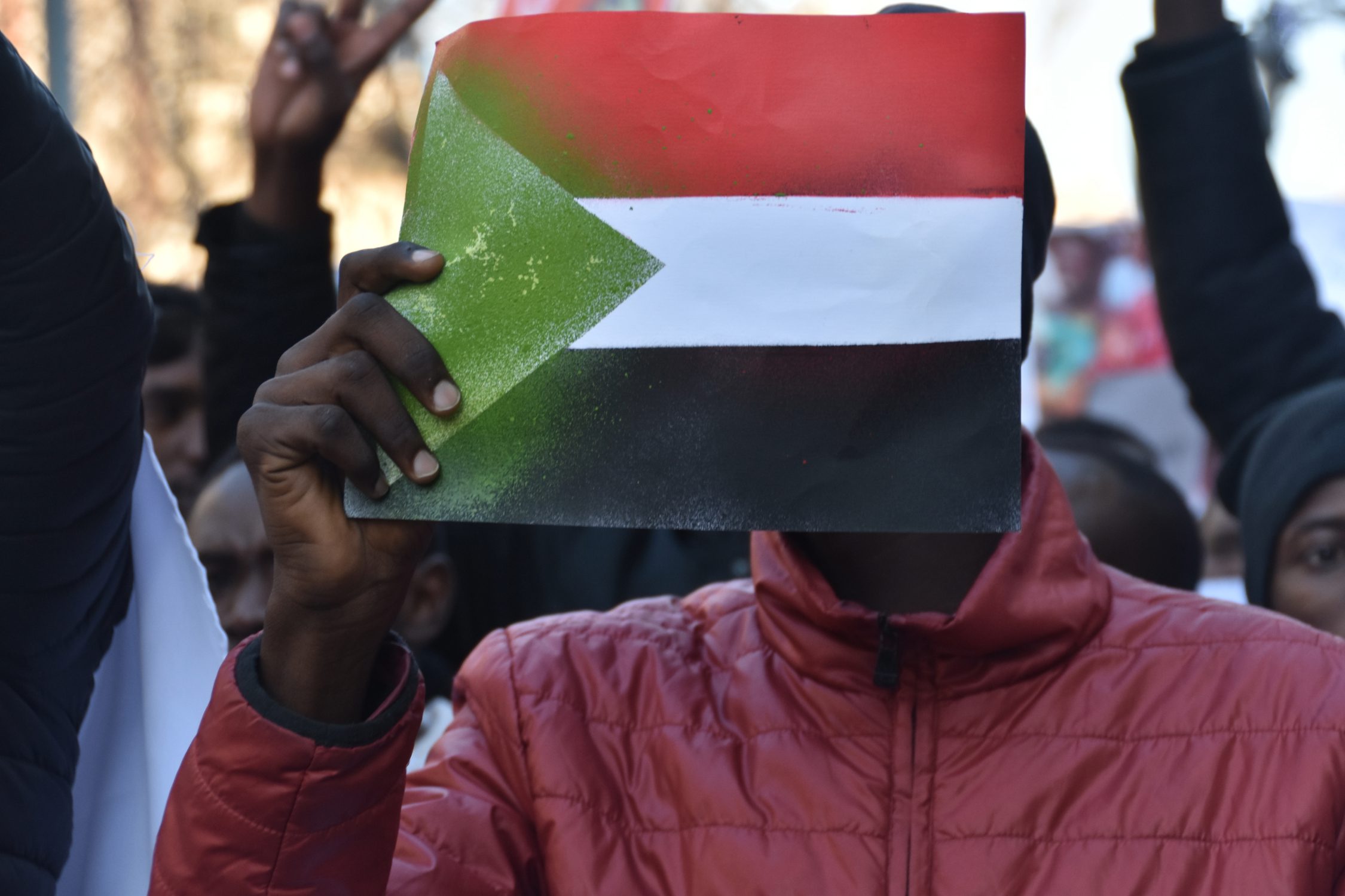 A peaceful protester holds in front of his face a sign representing the Sudanese flag