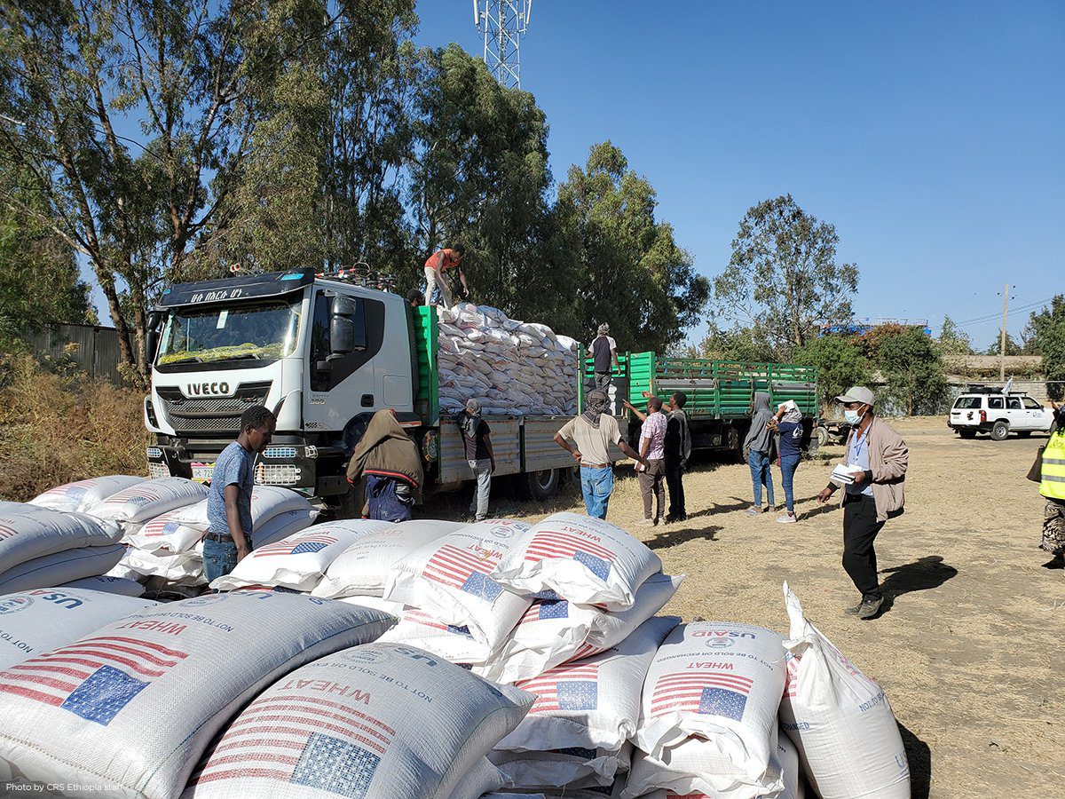 A group of men stand around a large truck delivering bags of wheat with the US flag logo