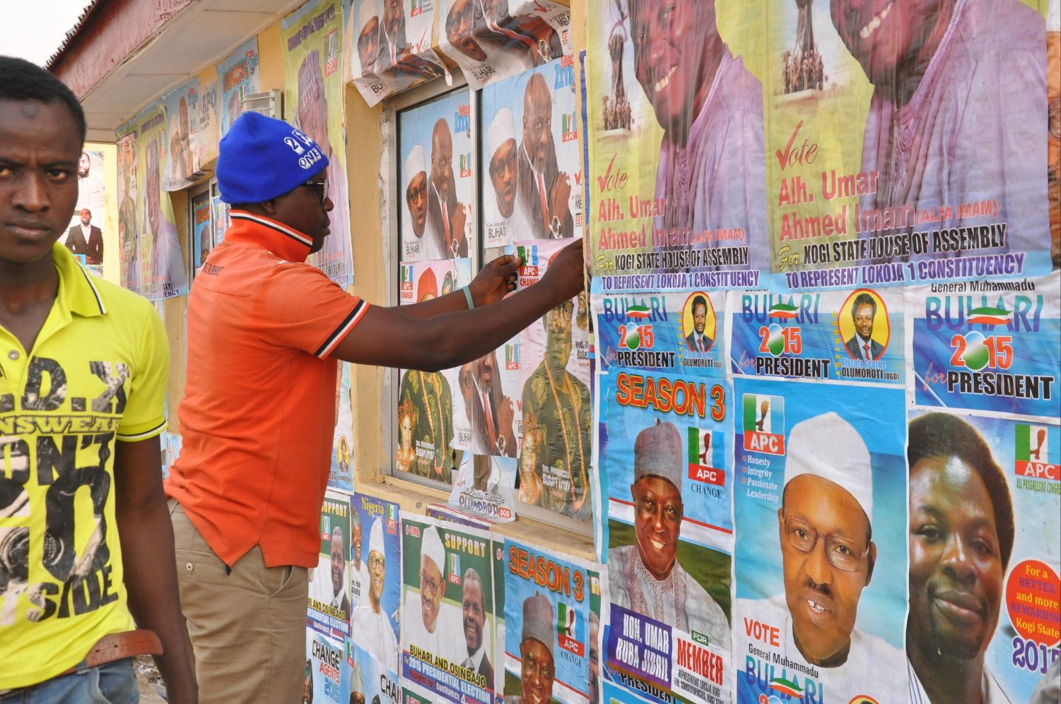 A man adds Nigerian election candidate posters to a wall covered with political posters
