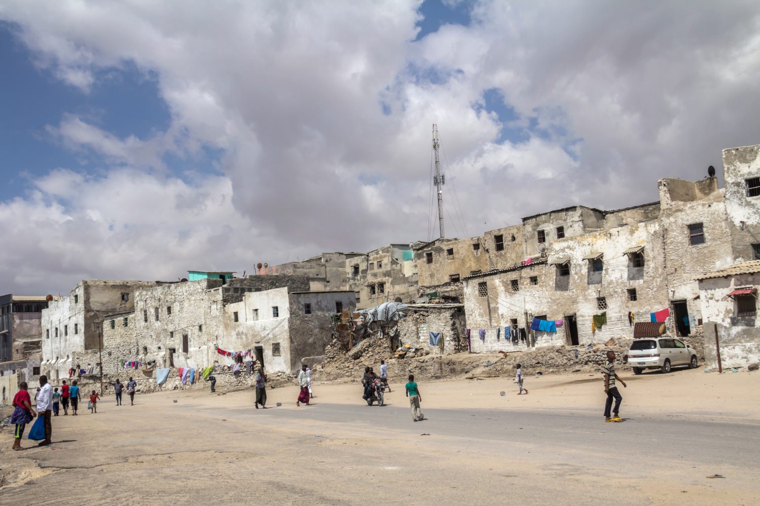 photo view of rundown buildings, dirt road with a few people walking around