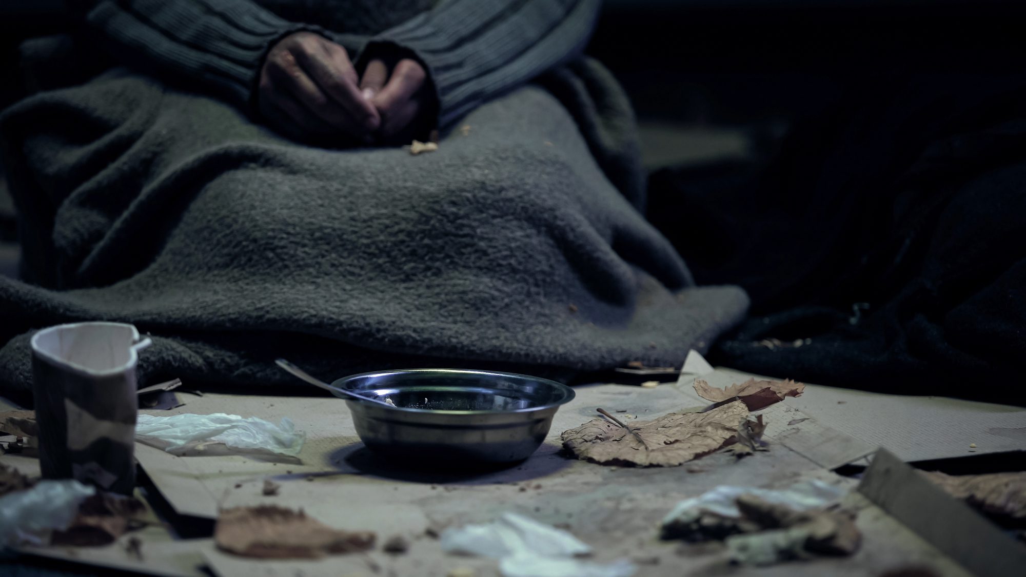 Poor person in dirty cloth sitting front of bowl, living on street