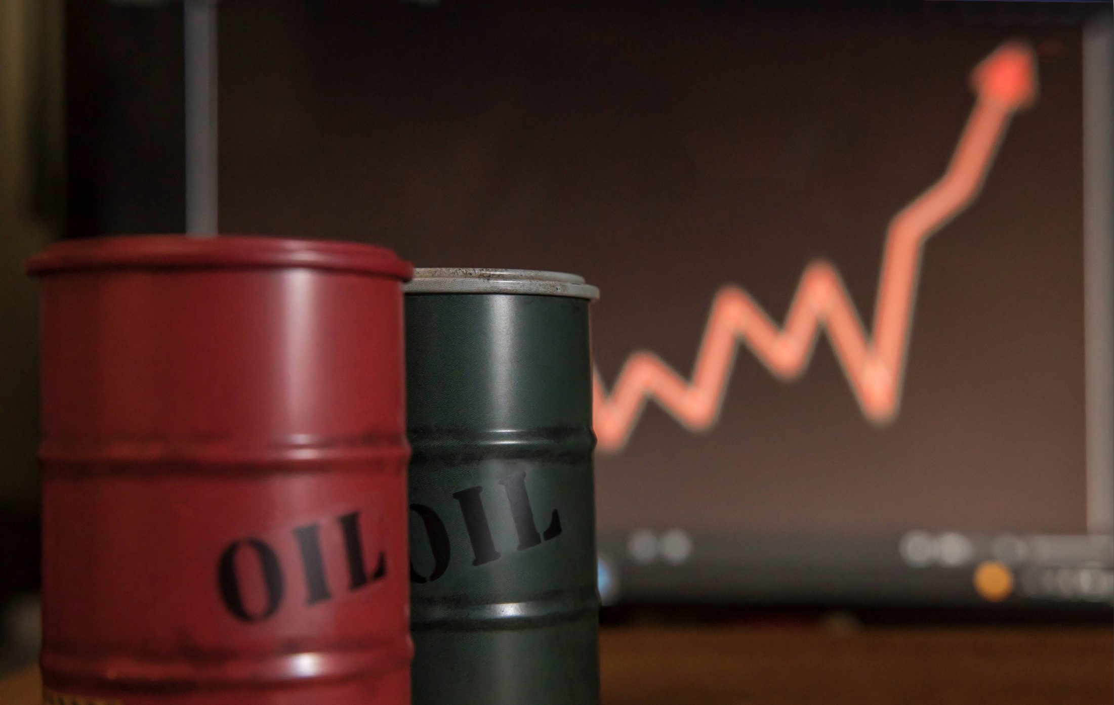Oil barrels in the foreground and a bullish chart in the background. Petroleum prices are rising